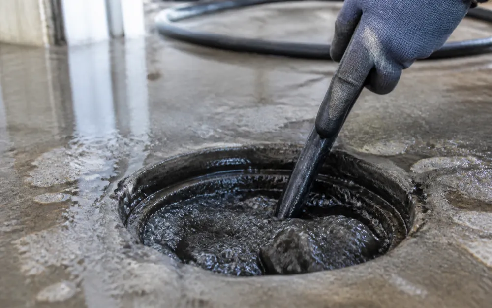 A hydro jetting hose fed into an open floor cleanout with dark water surging back up around it