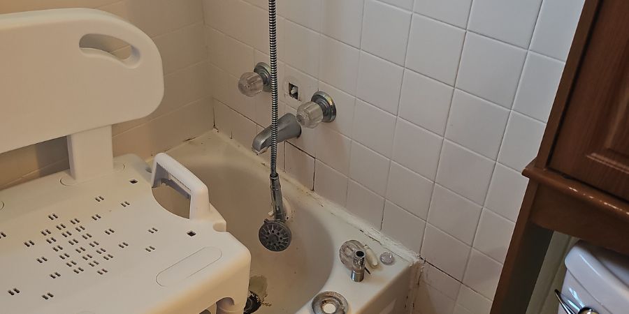 Clean white bathroom with bathtub, toilet, and white tile walls showing proper bathroom plumbing maintenance