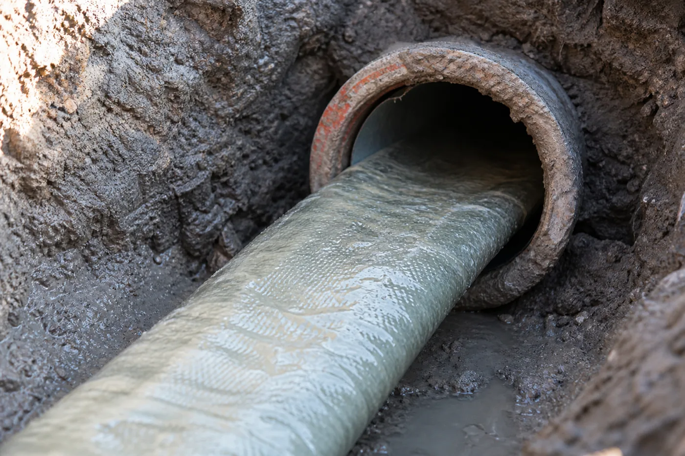 A trenchless pipe liner feeding into the exposed end of an underground pipe