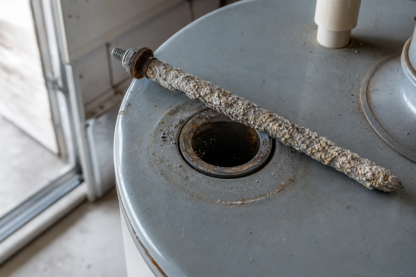 A heavily corroded sacrificial anode rod laid across the open top port of a residential water heater