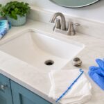 Bathroom sink with stopper removed, gloves, towels, and plastic drain tool for clearing a slow sink drain.