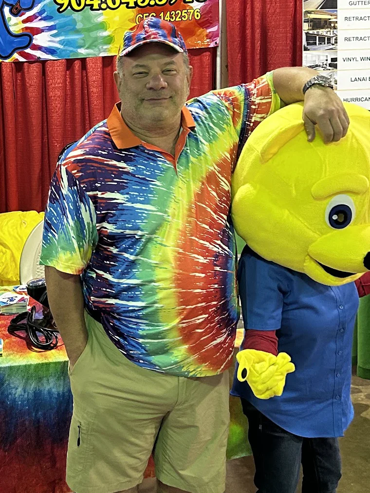 Steve Mandelbaum, founder of The Greatful Plumber, in a tie-dye shirt beside the company bear mascot at a Jacksonville home show